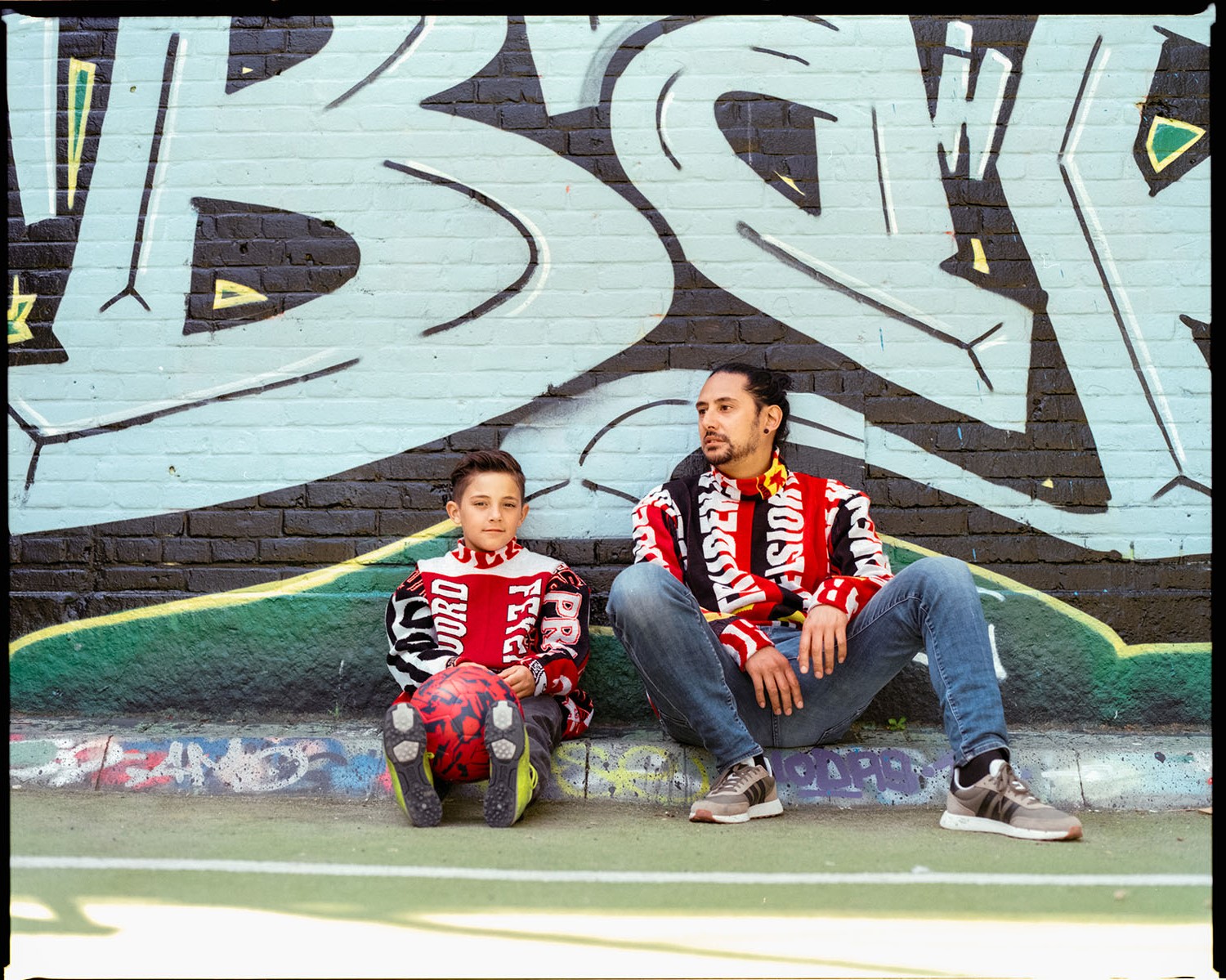 Man and kid posing against wall wearing different colored together sweaters